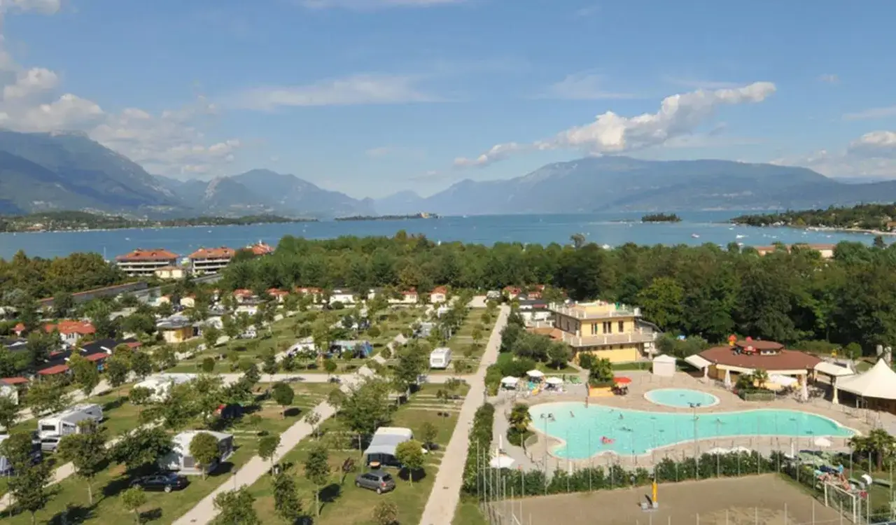 Widok na camping Baia Verde z kamperami, basenem i jeziorem w tle.
