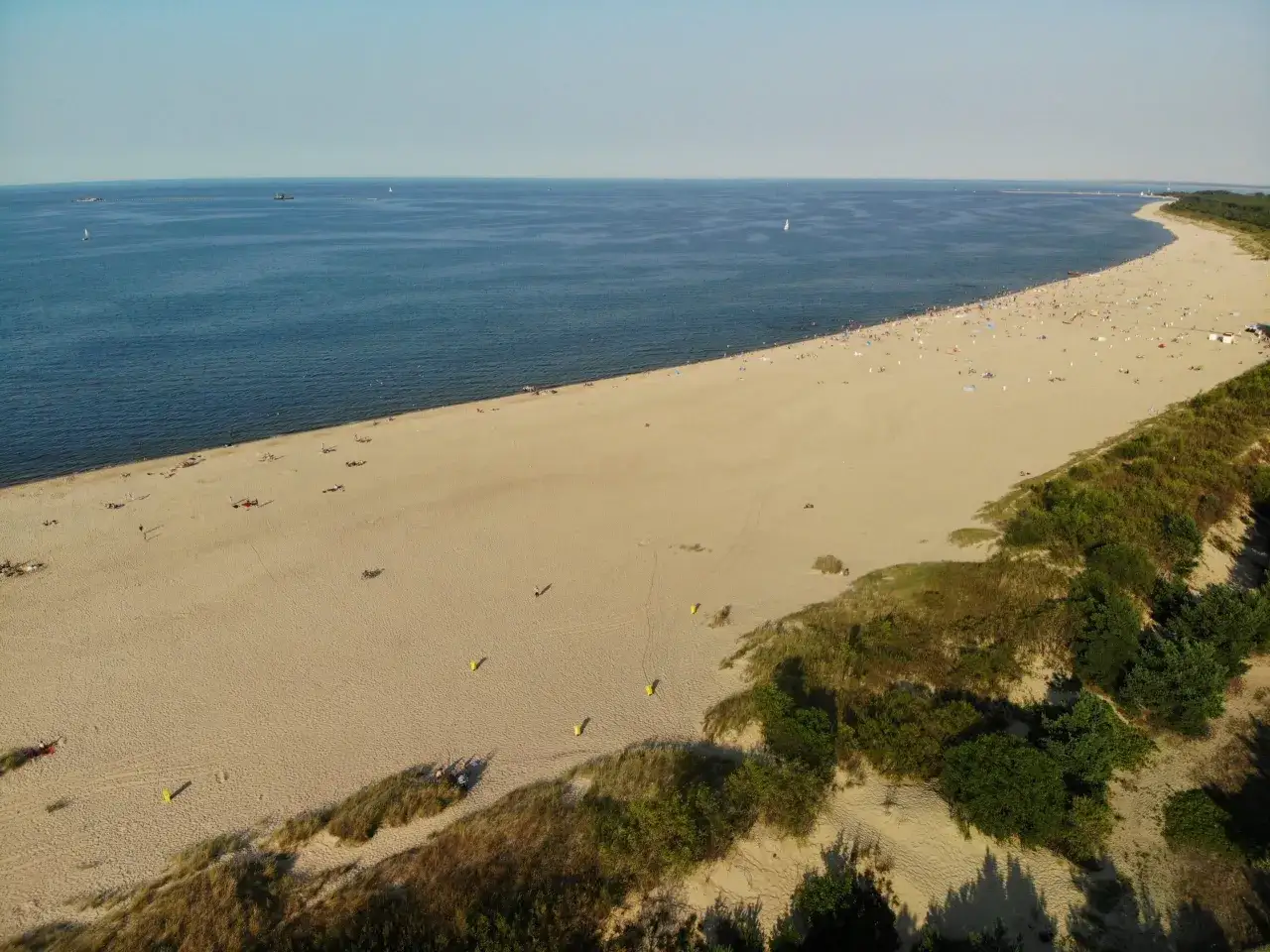 Szeroka, piaszczysta plaża z turystami i zielonymi wydmami. Idealne miejsce, gdzie warto pojechać nad morze na relaks.