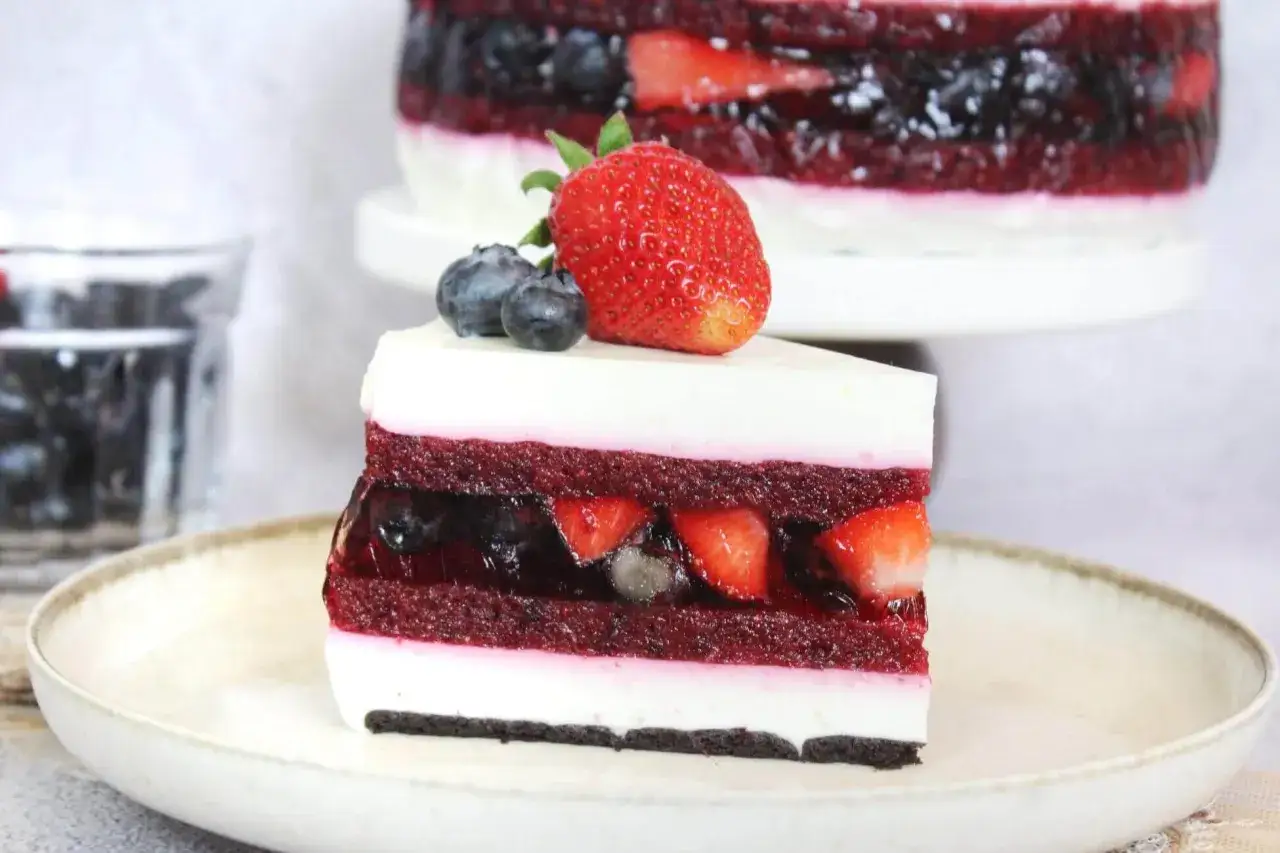 Sernik na zimno z galaretką, przełożony warstwami ciasta, owoc&oacute;w i kremu. Udekorowany truskawką i bor&oacute;wkami.