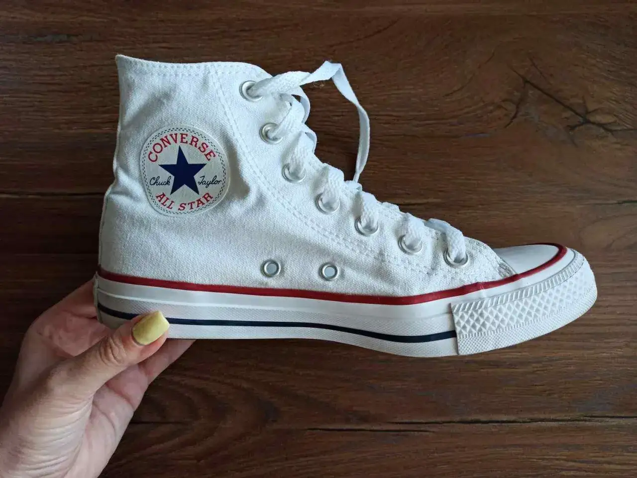 Białe trampki Converse na drewnianym tle. Dowiedz się, jak prać Conversy w pralce, by znów lśniły czystością.