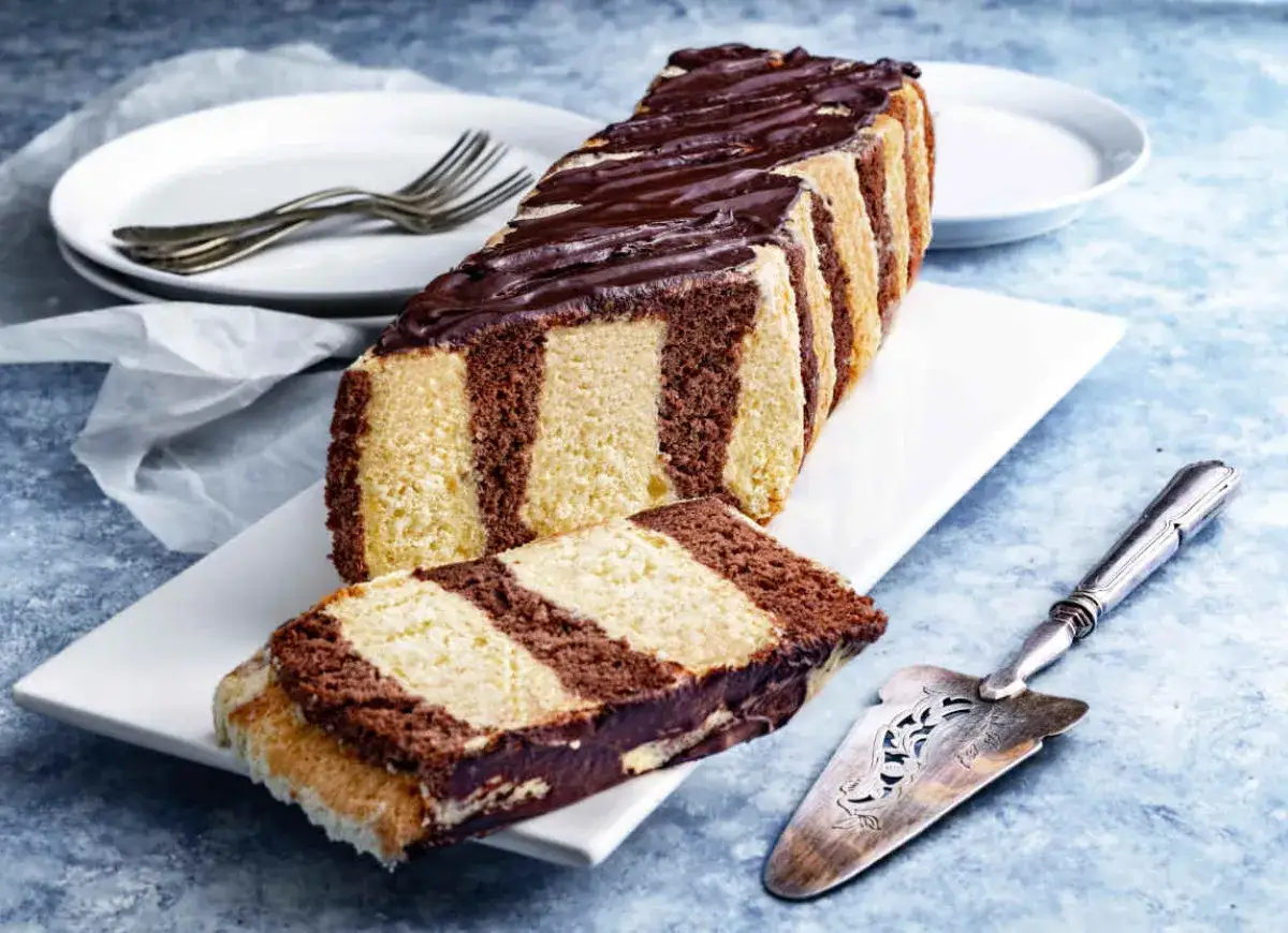 Ciasto metrowiec stary przepis. Paski jasnego i ciemnego ciasta, polane czekoladą, na białej paterze.