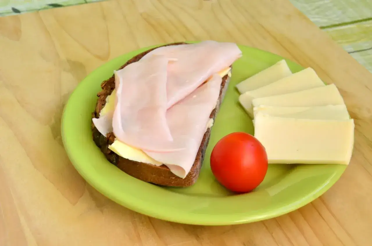 Kanapka z szynką i serem na zielonym talerzu. Zielonkawy połysk na wędlinie może oznaczać, że jest świeża i można ją bezpiecznie zjeść.