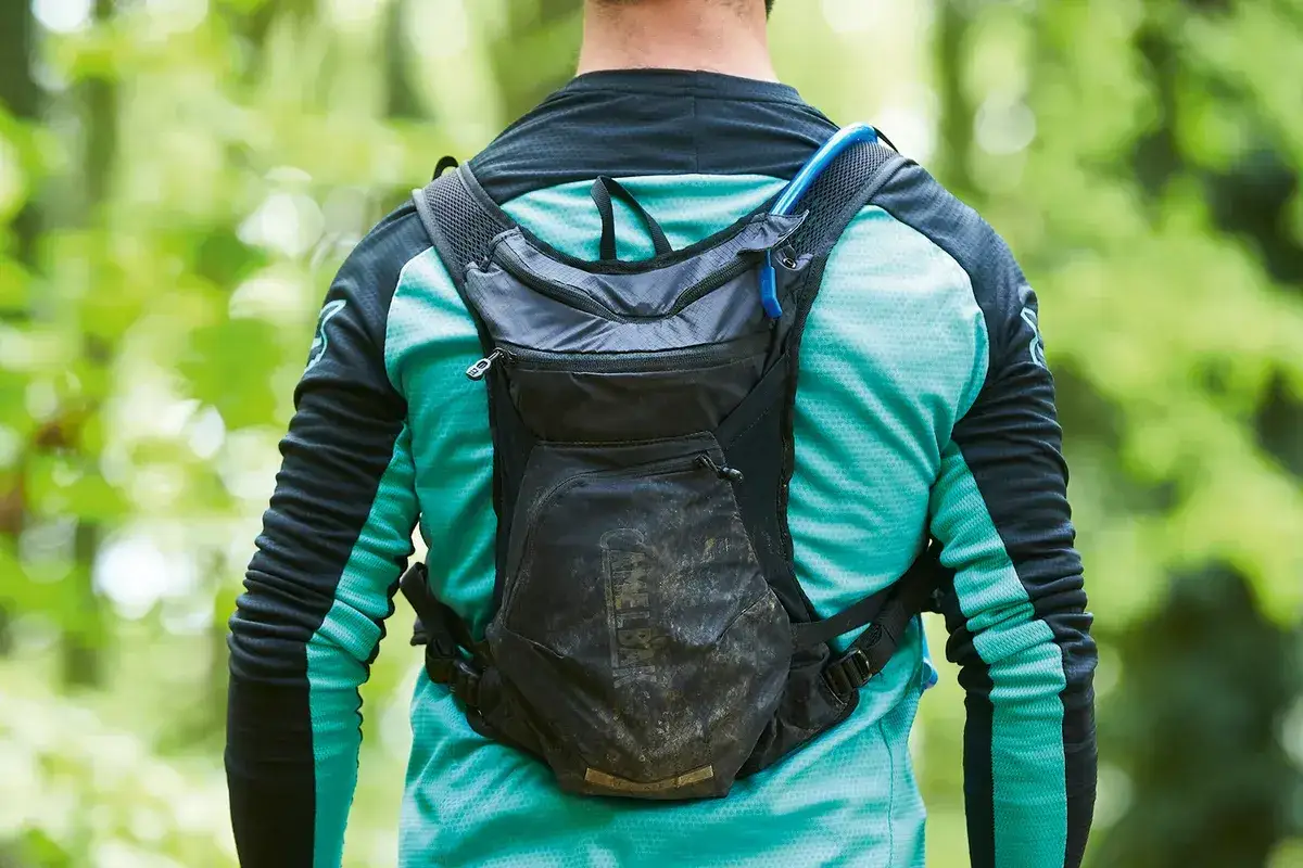 Rowerzysta w błotnistym plecaku Camelbak, gotowy na 100 km na rowerze przez leśne ścieżki.