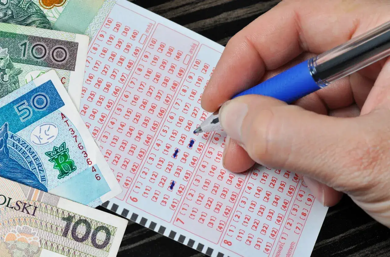 Dłoń zaznacza liczby na kuponie lotto. Obok leżą polskie banknoty. Czy nagroda w loterii pożyczkowej jest zwolniona z podatku od wzbogacenia?