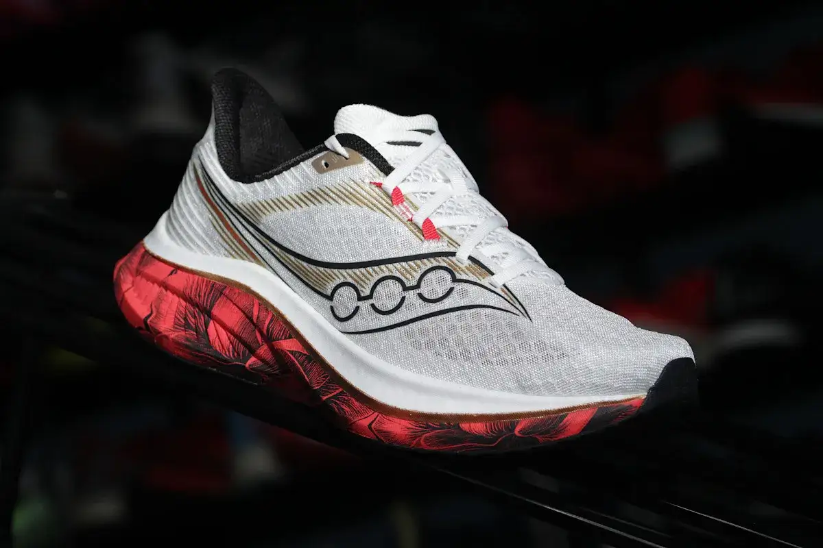 Białe buty do biegania z czerwono-czarną podeszwą i złotymi detalami. Idealne buty supinujące dla biegaczy.