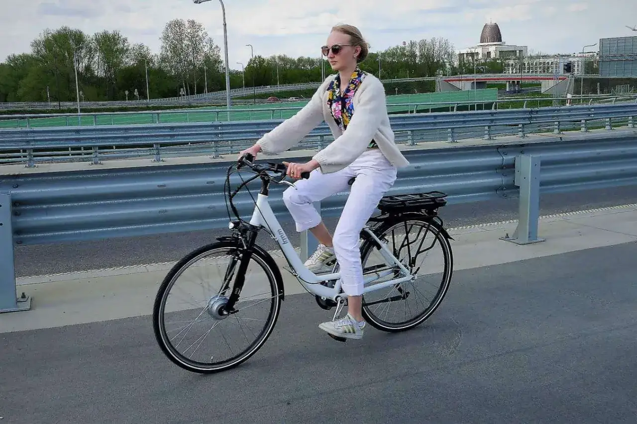 Kobieta na białym, najmocniejszym rowerze elektrycznym jedzie po moście.