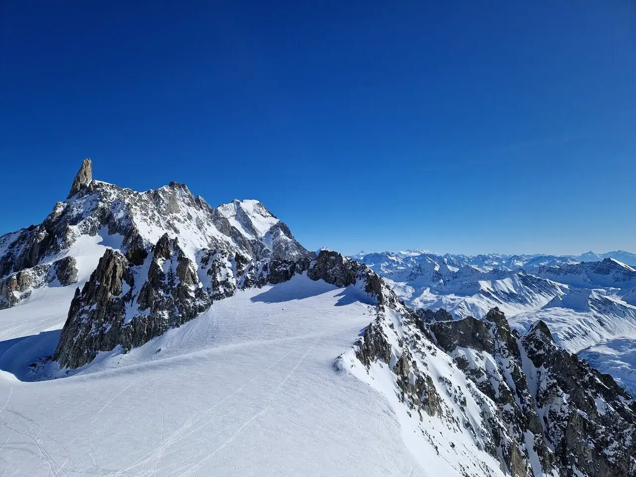 Majestatyczny Mont Blanc w śnieżnej koronie, otoczony skalistymi szczytami i błękitem nieba. Widok zapiera dech w piersiach.