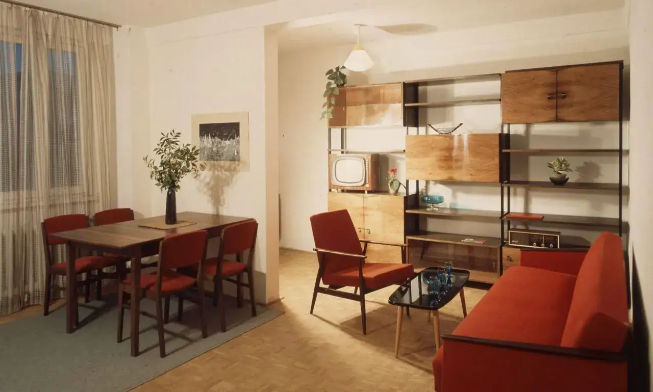 Wnętrze po renowacji mebli PRL: jadalnia z drewnianym stołem i krzesłami, salon z regałem, fotelem i kanapą w kolorze ceglastym.