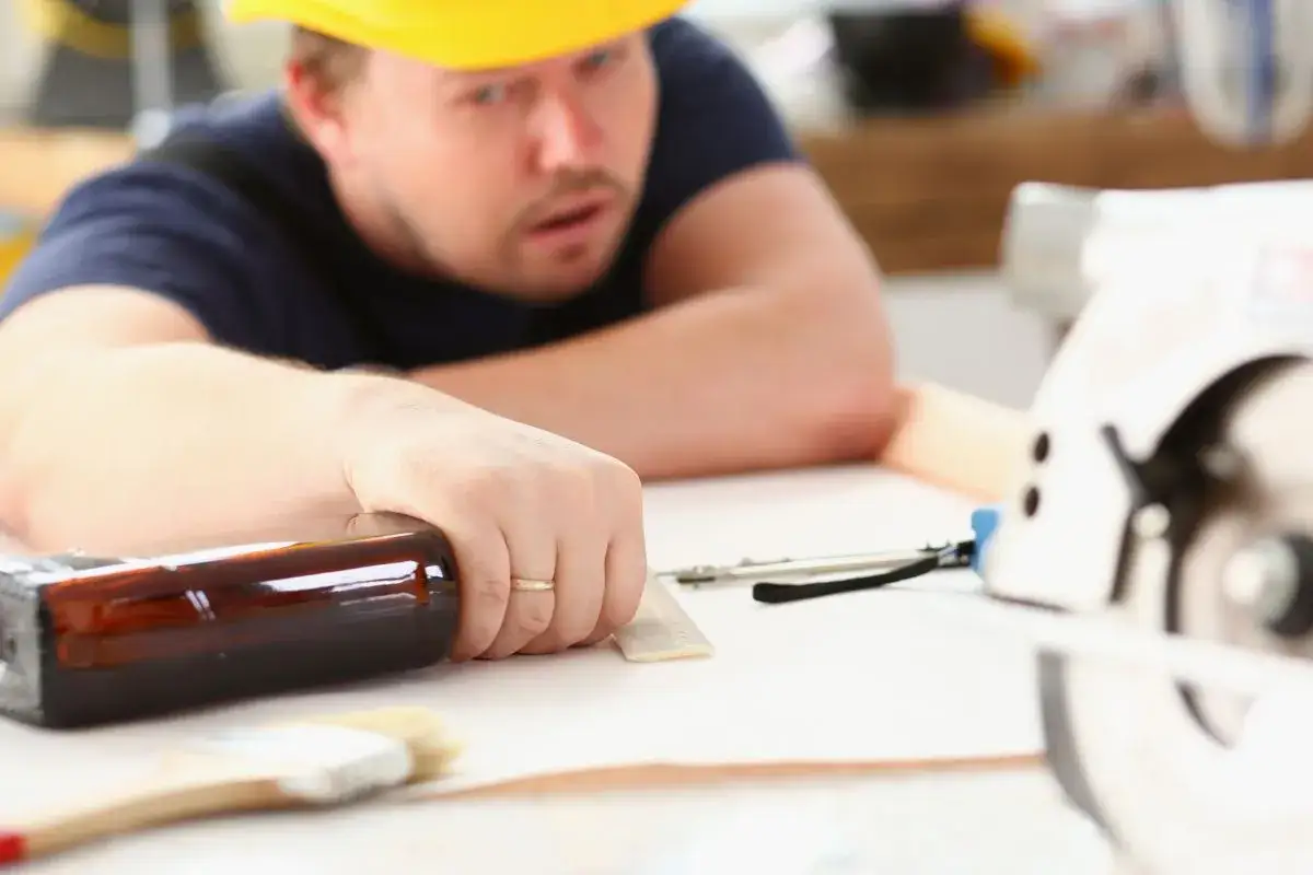 Pracownik w żółtym kasku, z butelką w dłoni, zastanawia się, czy pracodawca może sprawdzić pracownika alkomatem.