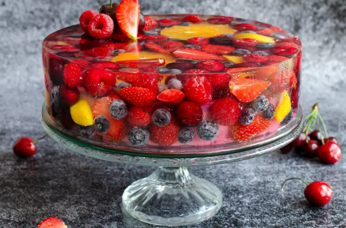 Sernik na zimno z galaretką, pełen truskawek, malin, bor&oacute;wek i pomarańczy, prezentuje się jak letni ogr&oacute;d w deserze.