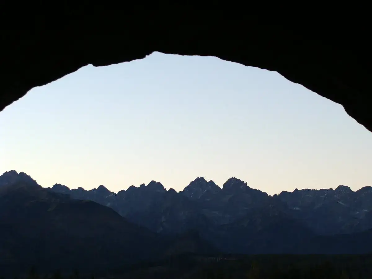Widok na g&oacute;ry z jaskini. G&oacute;ry rysują się na tle jasnego nieba, jakby były domem na wierchu świata.