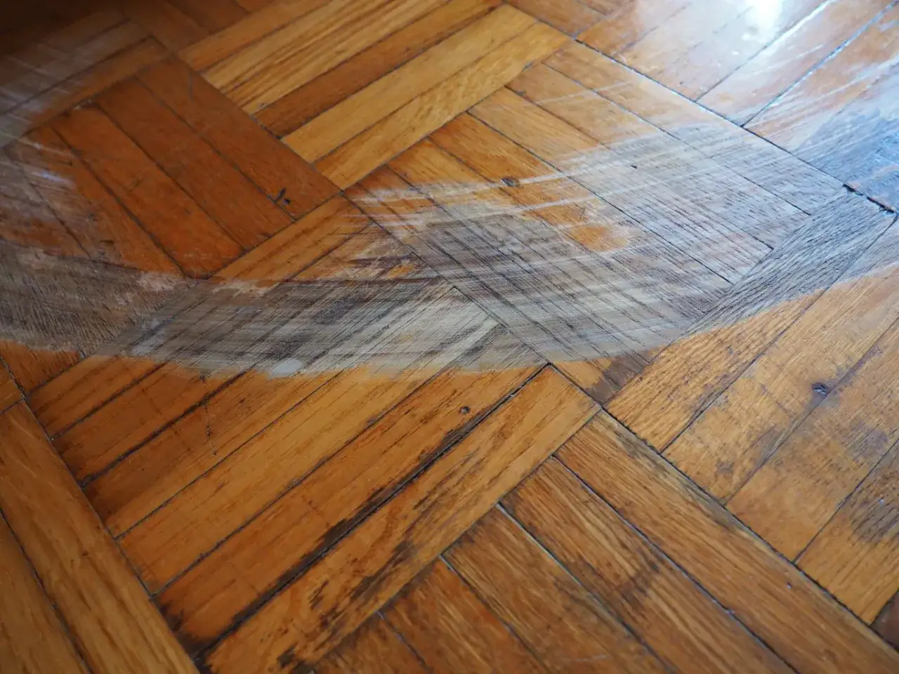 Widoczne ślady po miejscowej naprawie podłogi drewnianej. Widać r&oacute;żnicę w odcieniu i fakturze drewna po pracach renowacyjnych.