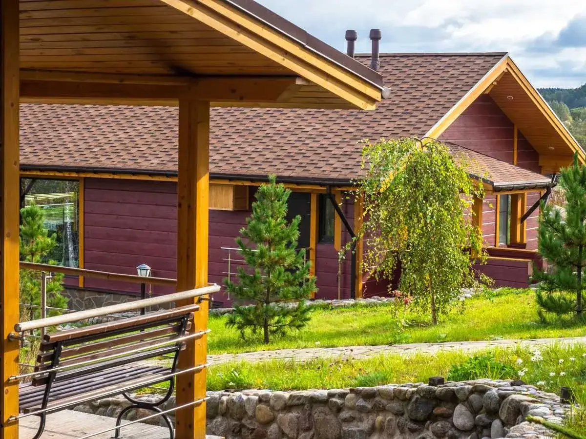 Drewniany domek z czerwoną elewacją i brązowym dachem. Idealne miejsce, by znaleźć tanie noclegi w Polsce i odpocząć na łonie natury.