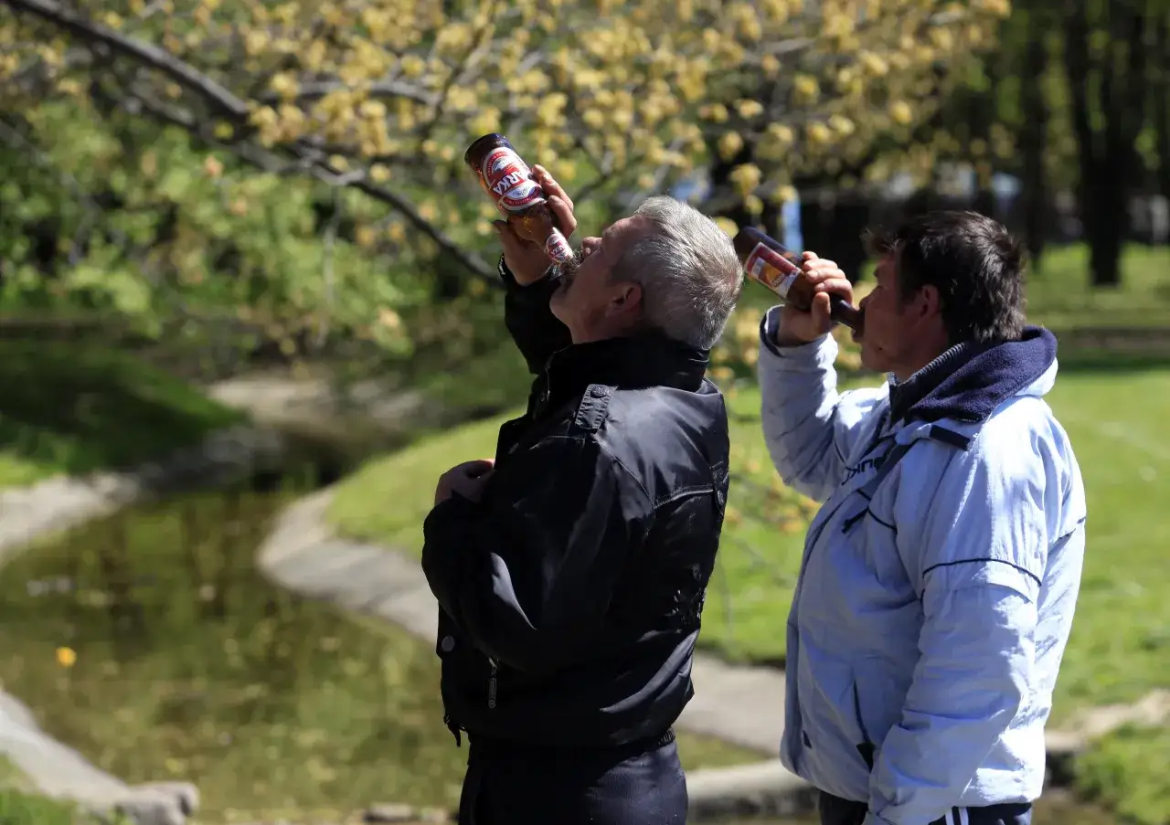 Dwóch mężczyzn pije piwo w parku. Czy we Francji można pić w miejscu publicznym? To zależy od regionu i lokalnych przepisów.