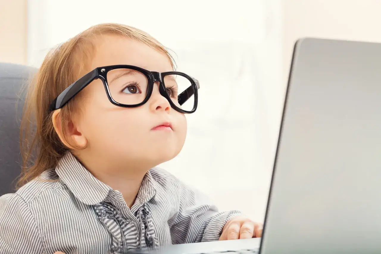 Małe dziecko w okularach z astygmatyzmem 0.5 zastanawia się, czy nosić okulary, patrząc na laptopa.