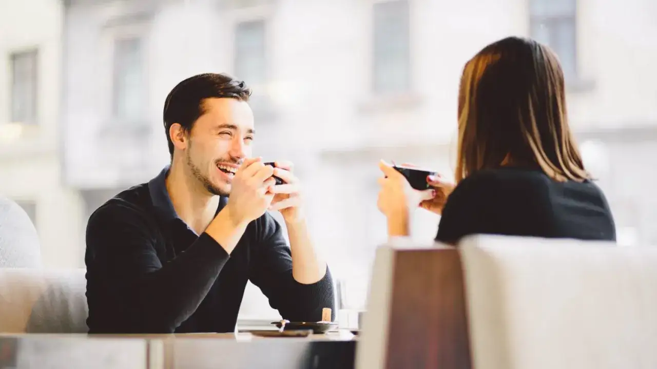 Uśmiechnięty mężczyzna podczas randki z kobietą, trzymający filiżankę.