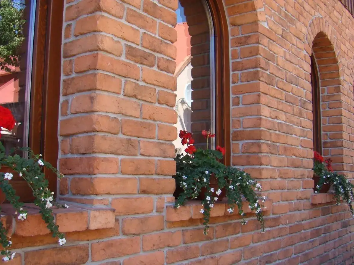 Elewacja z klinkieru z ozdobnymi okiennicami i kwitnącymi pelargoniami.