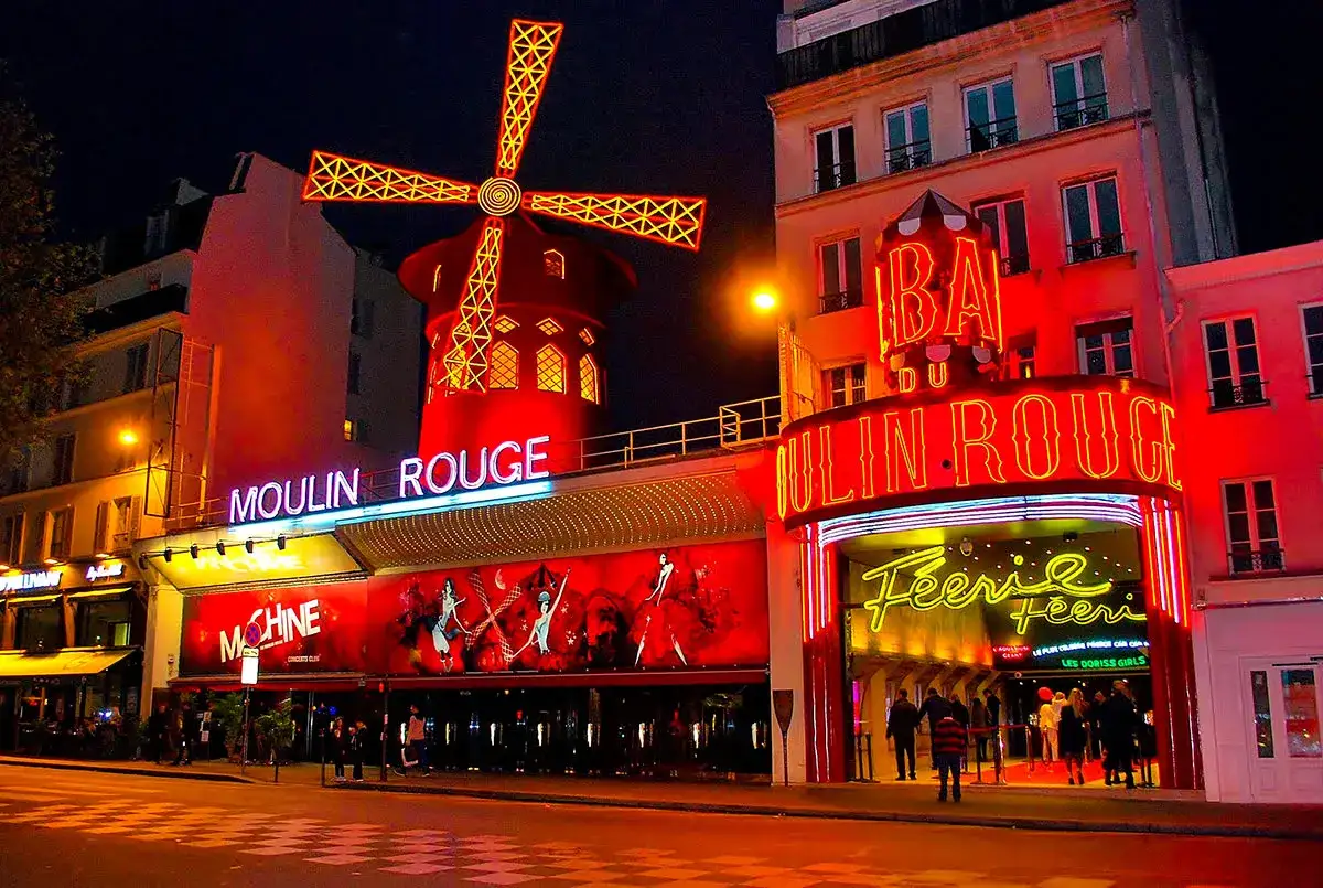 Nocne światła rozświetlają słynny Moulin Rouge w 18 dzielnicy Paryża. Neonowy wiatrak i napisy zapraszają do legendarnego kabaretu.