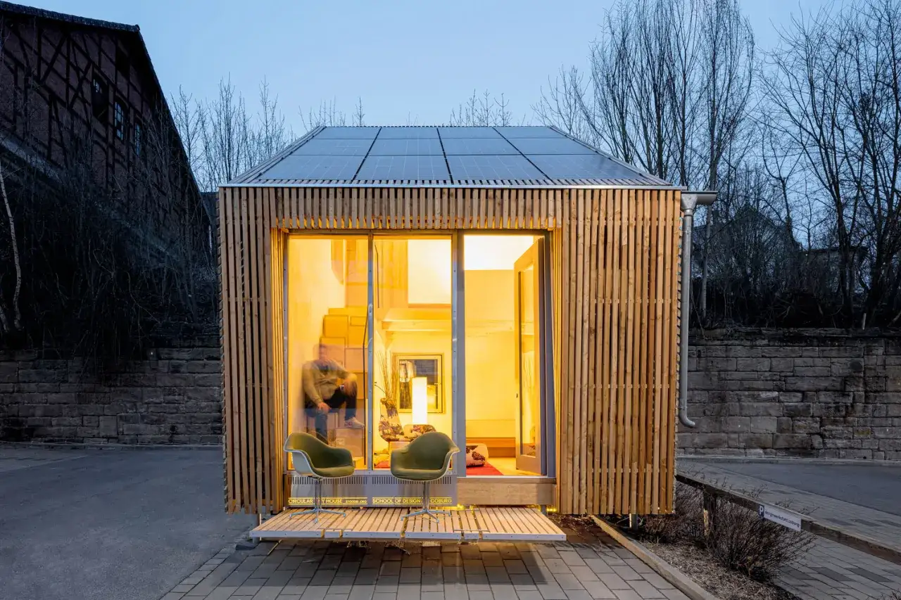 Najmniejszy dom na świecie, z panelami słonecznymi na dachu i drewnianą elewacją, zaprasza do przytulnego wnętrza.