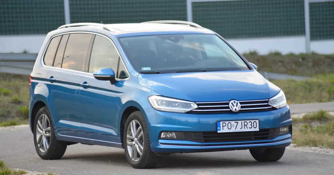 Niebieski Volkswagen Touran z relingami dachowymi, zaparkowany na drodze.