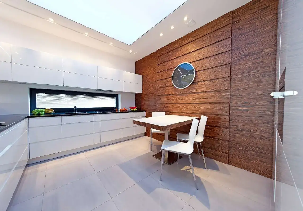 Nowoczesna kuchnia z białymi frontami i drewnianymi panelami na ścianach. Stół z krzesłami czeka na posiłek.