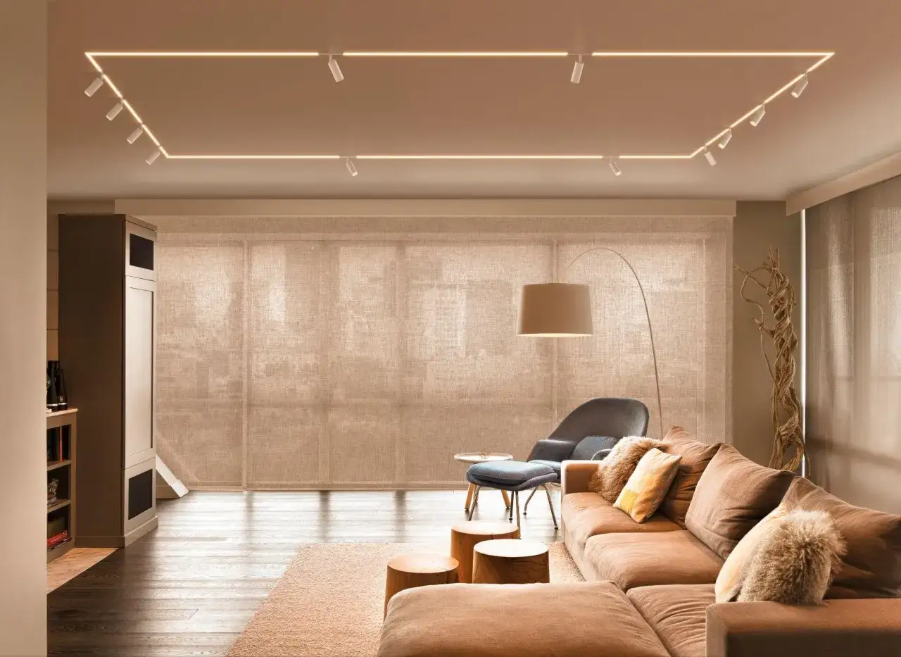 Nowoczesne punkty świetlne sufitowe tworzą ramę dla przytulnego salonu z brązową kanapą i drewnianymi stołkami.