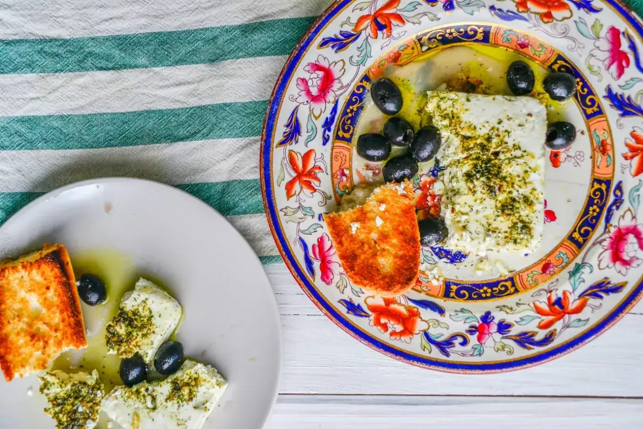 Ser feta z oliwkami i grzankami na ozdobnym talerzu. Proste, pyszne greckie przepisy na letni obiad.