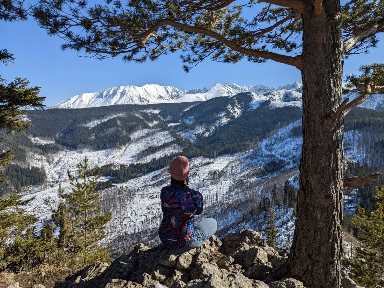 Osoba siedzi na skale, podziwiając zimowy krajobraz Tatr. Szlak na Nosal wita pięknymi widokami.