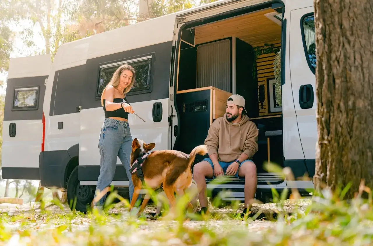 Para odpoczywa przy swoim kamperze, bawiąc się z psem.