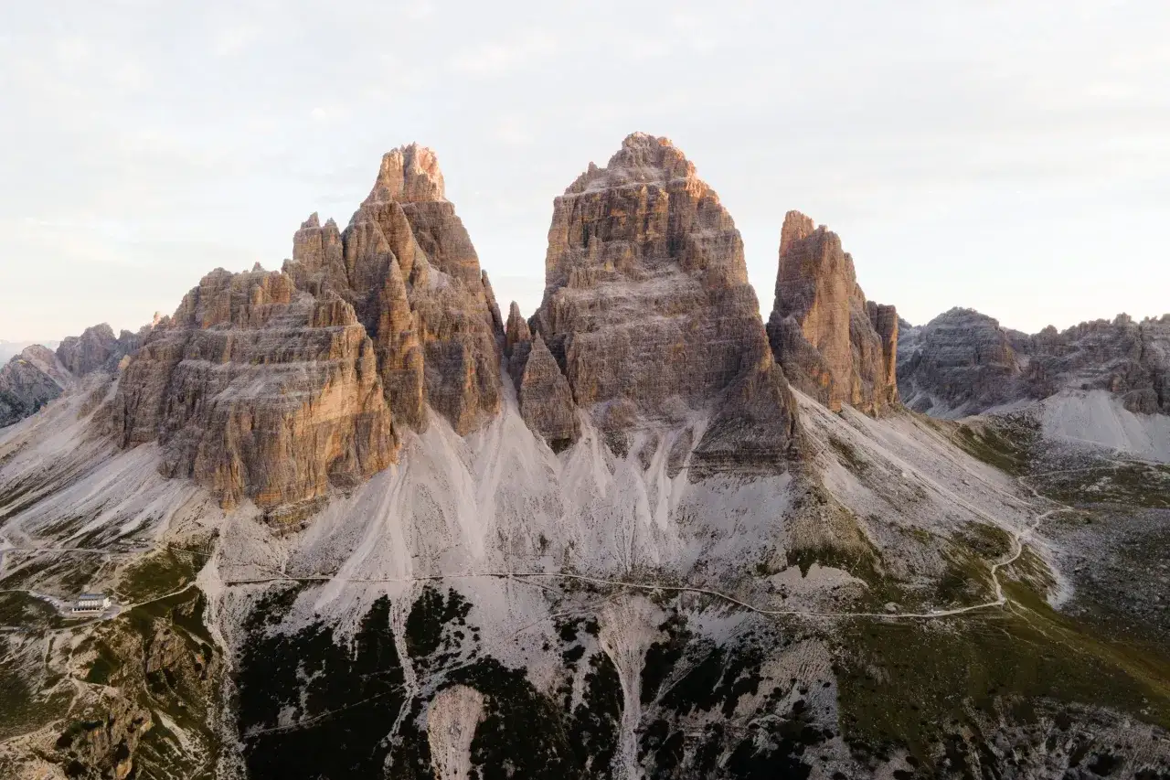 Majestatyczne szczyty Tre Cime di Lavaredo o wschodzie słońca, z widocznym schroniskiem i krętymi ścieżkami.