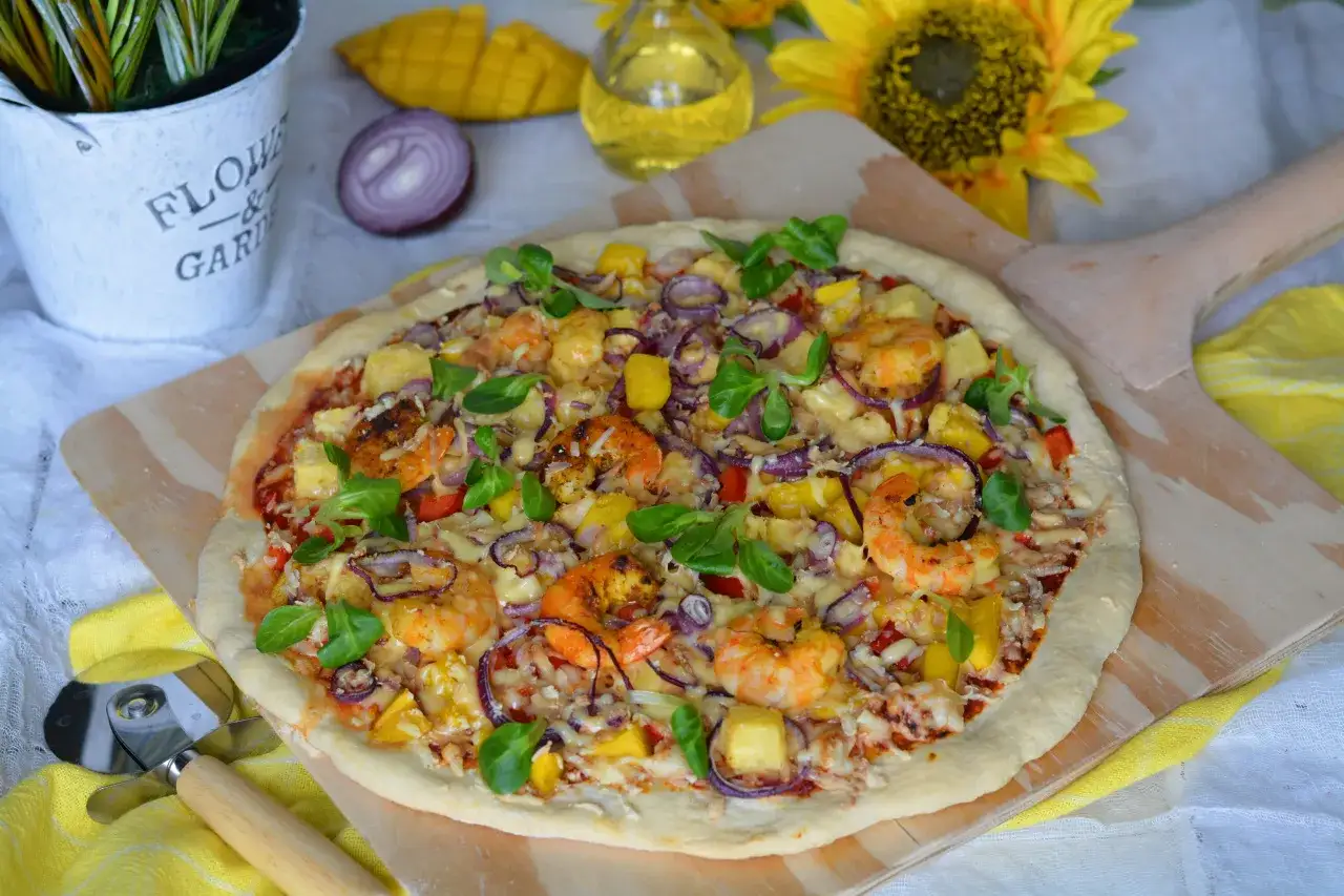 Pyszna pizza z krewetkami, ananasem i czerwoną cebulą, udekorowana świeżymi listkami.