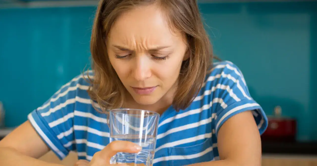 Kobieta z grymasem na twarzy trzyma szklankę wody, czując gorzki smak w ustach.