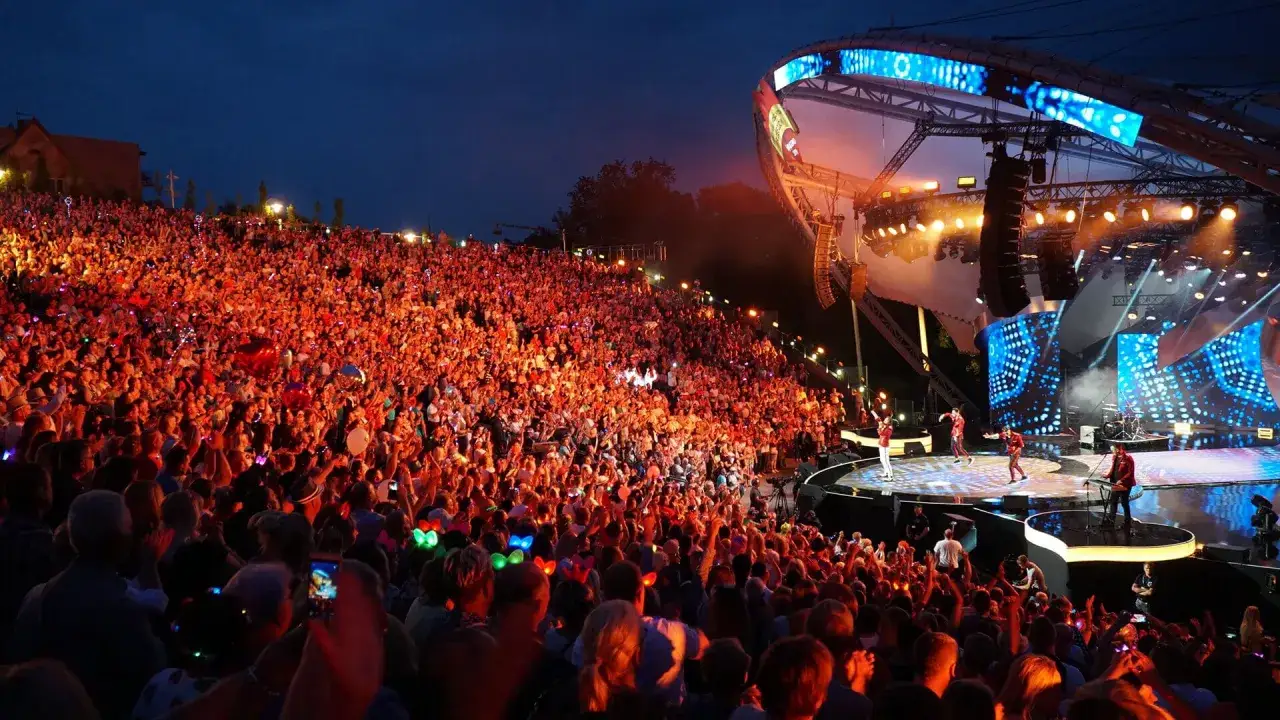 Koncert w amfiteatrze w Mrągowie. Tłumy widzów, artyści na scenie, światła i muzyka tworzą niezapomniane mrągowo atrakcje.