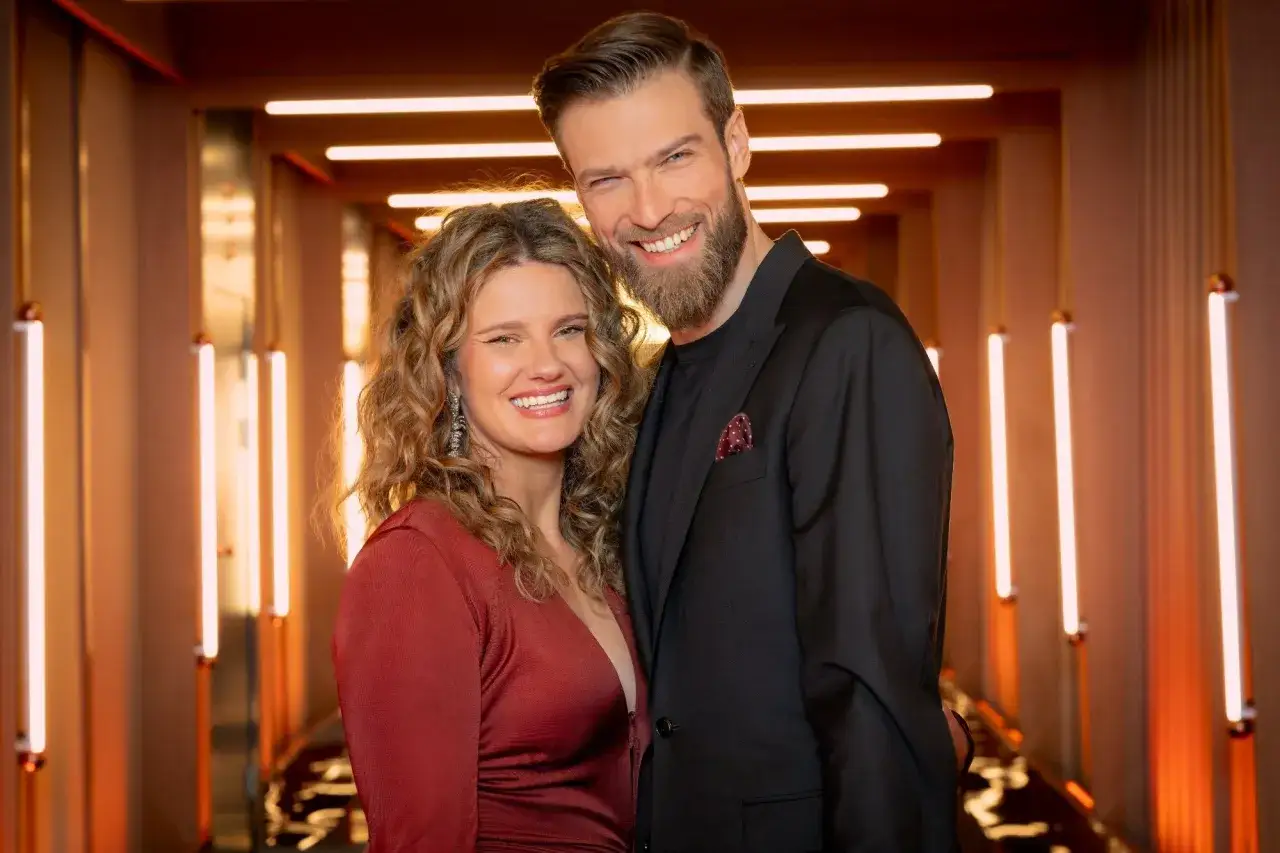 Uśmiechnięta para, ona w czerwonej sukience, on w czarnym garniturze, na tle neonowych świateł. Czy to początek miłości ślepej w Polsce?