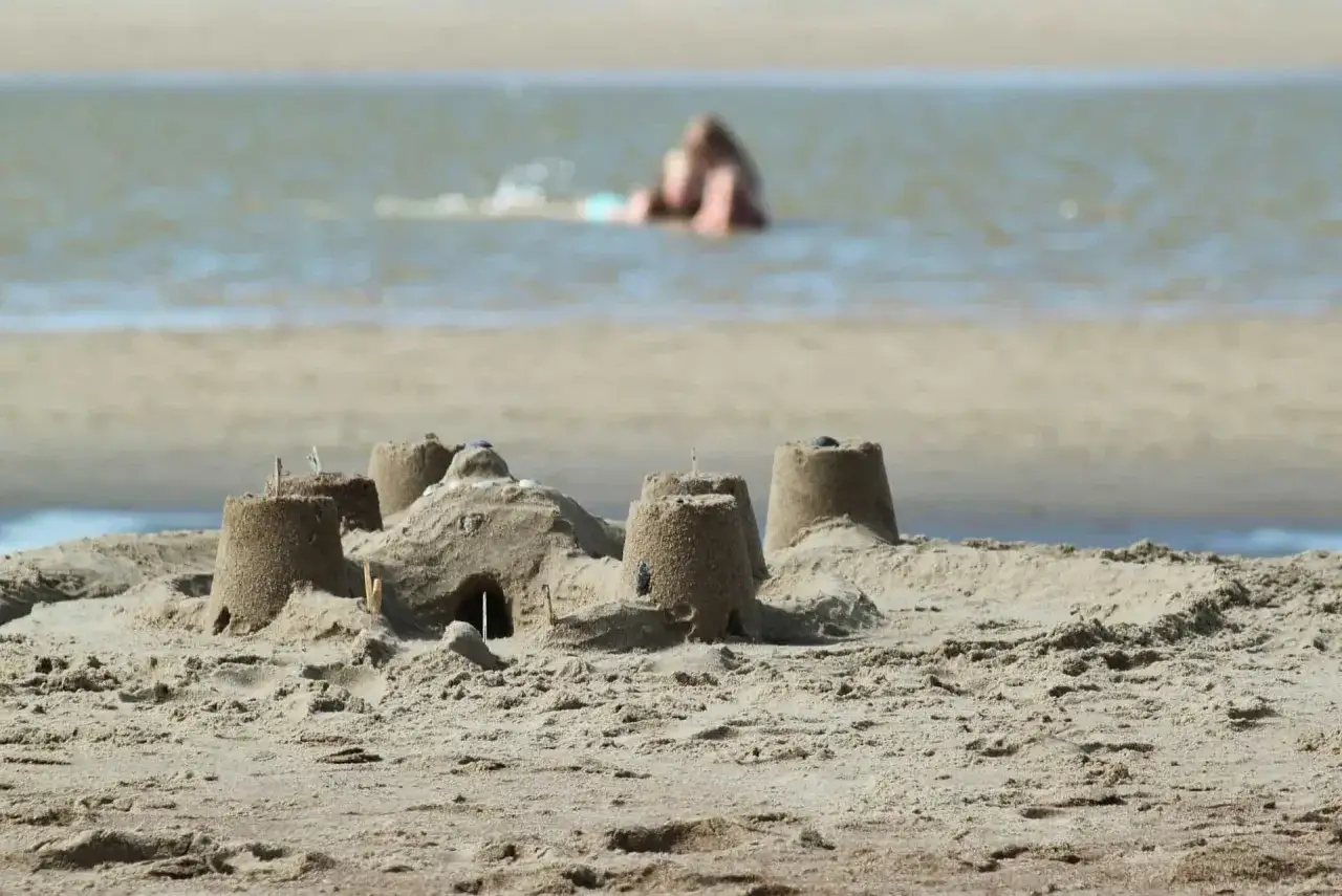 Zamek z piasku na plaży w Ciszycy, w tle osoba kąpiąca się w morzu.