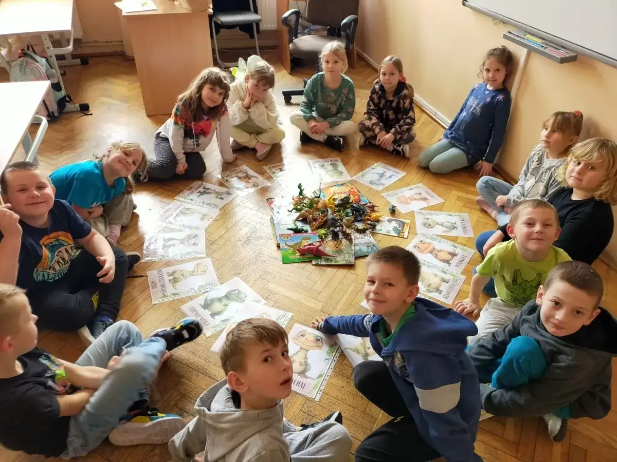Dzieci z zaciekawieniem oglądają obrazki z dinozaurami, tworząc świetny pomysł na gazetkę szkolną.