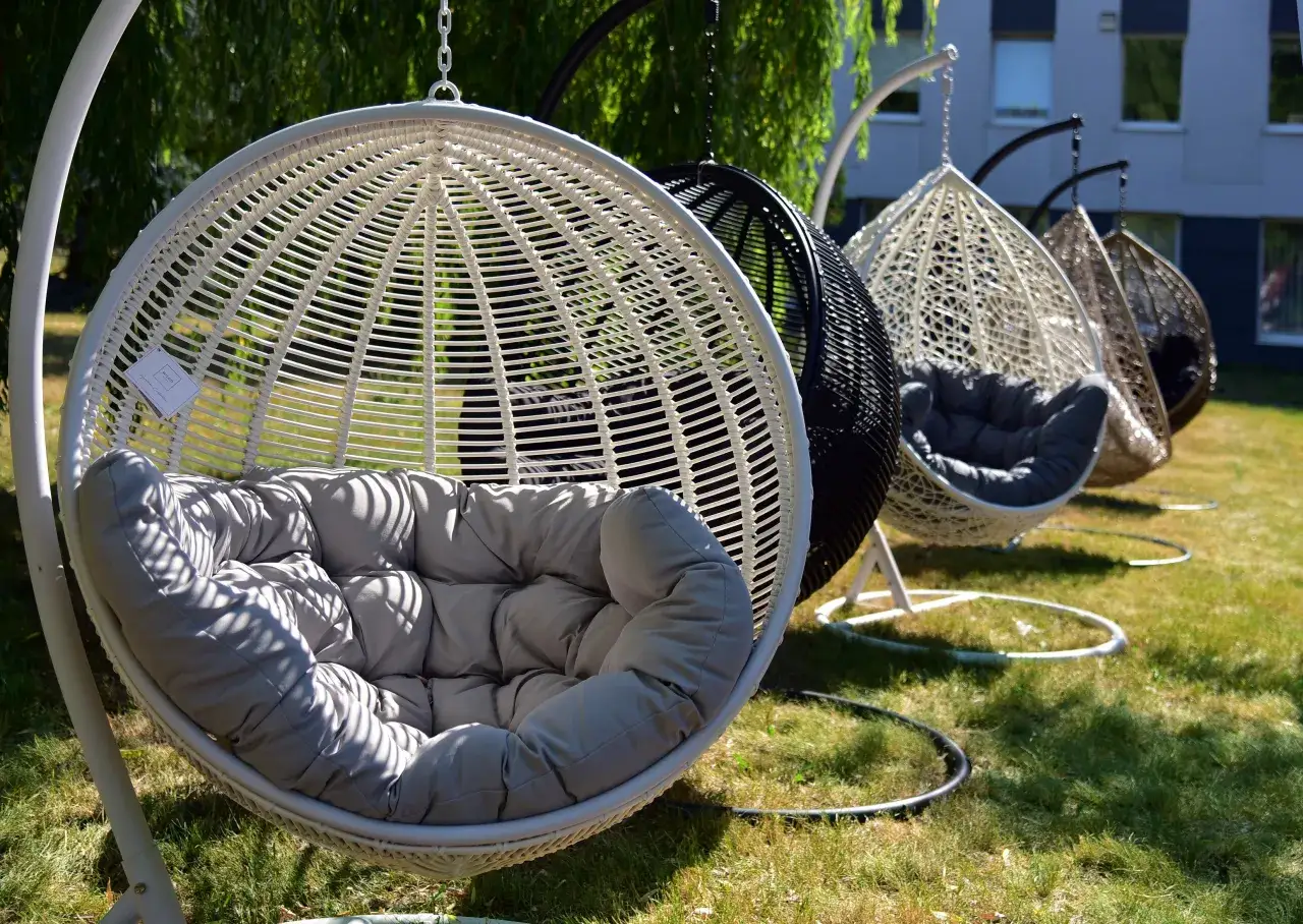 Kilka wiszących foteli w kształcie kokonu, z miękkimi poduszkami, ustawionych na trawie.