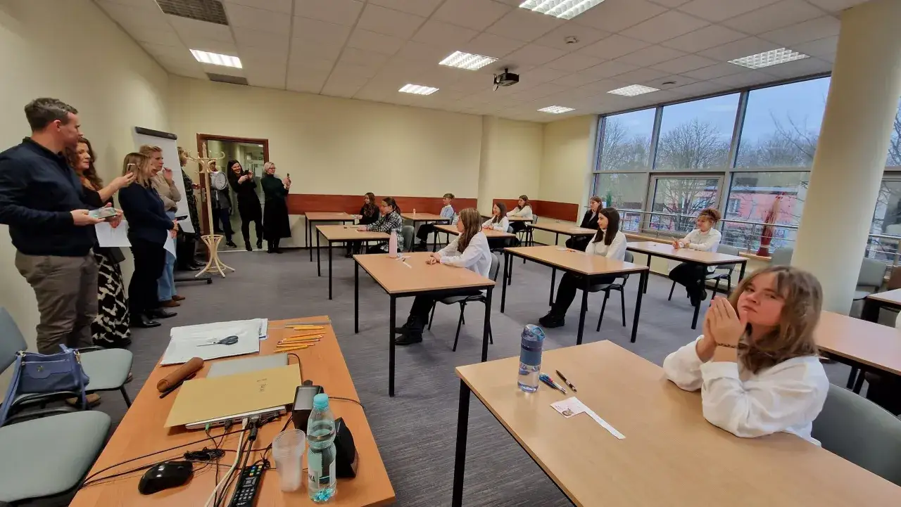 Uczniowie siedzą przy ławkach, gotowi do mscdn konkursy przedmiotowe. Nauczyciele obserwują ich z boku.