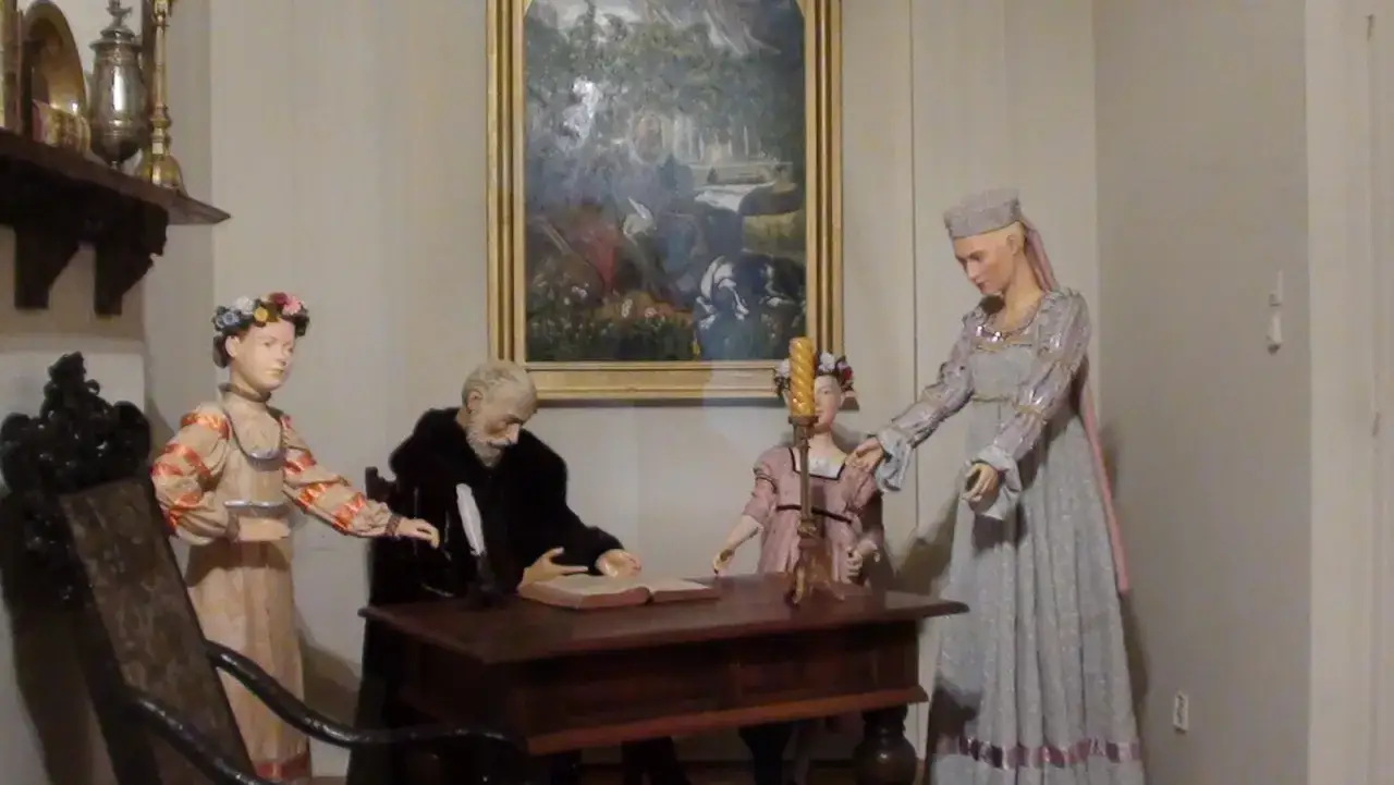 Scena z życia Jana Kochanowskiego w Czarnolesie: pisarz pochylony nad księgą, obok niego dzieci i dama.