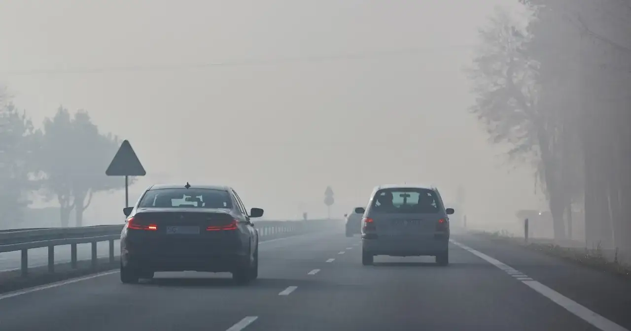 Mglisty poranek na drodze. Samochody jadą z włączonymi światłami mijania, by zapewnić widoczność.