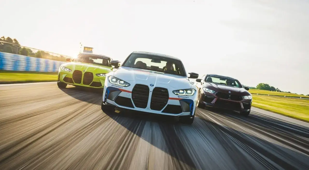Trzy BMW M3 G80 w różnych kolorach pędzą po torze wyścigowym.