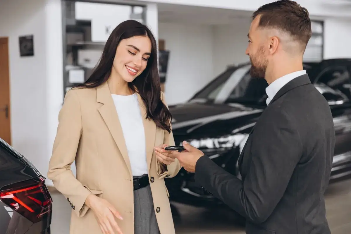 Uśmiechnięta kobieta odbiera kluczyki do nowego auta. Sprzedawca oferuje leasing bezpośredni, ułatwiając zakup.
