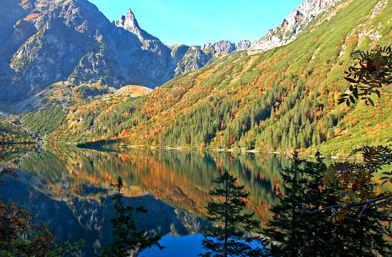 Jesienne Tatry zachwycają. Jezioro Morskie Oko odbija góry i lasy w jesiennych barwach, tworząc malownicze tatry atrakcje.