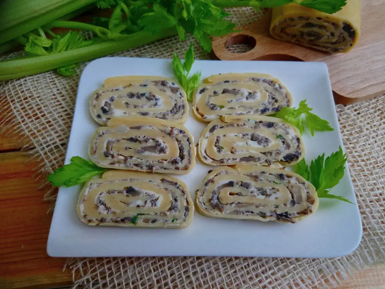 Rolada serowa z pieczarkami i ziołami, pokrojona na plastry, prezentuje się apetycznie na białym talerzu.