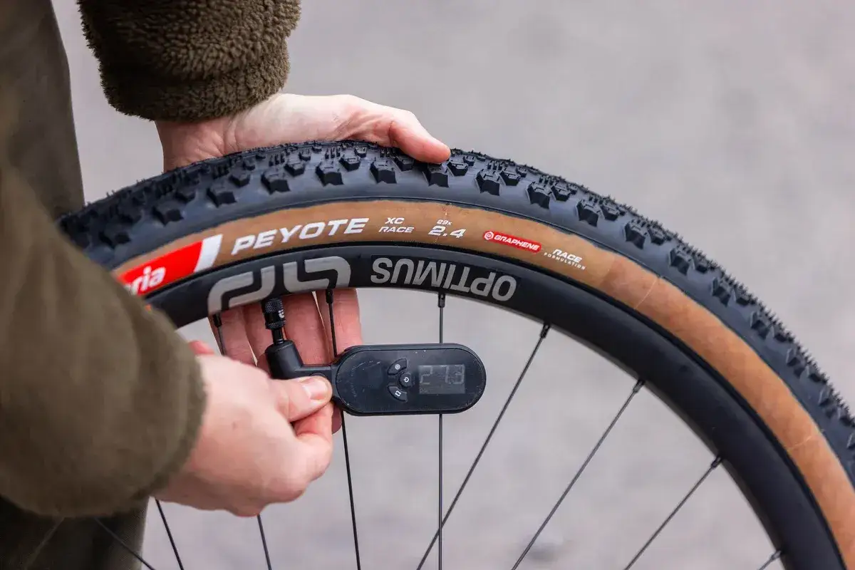 Sprawdzanie, jakie ciśnienie w rowerze g&oacute;rskim jest optymalne, za pomocą cyfrowego manometru. Na oponie widoczny napis 