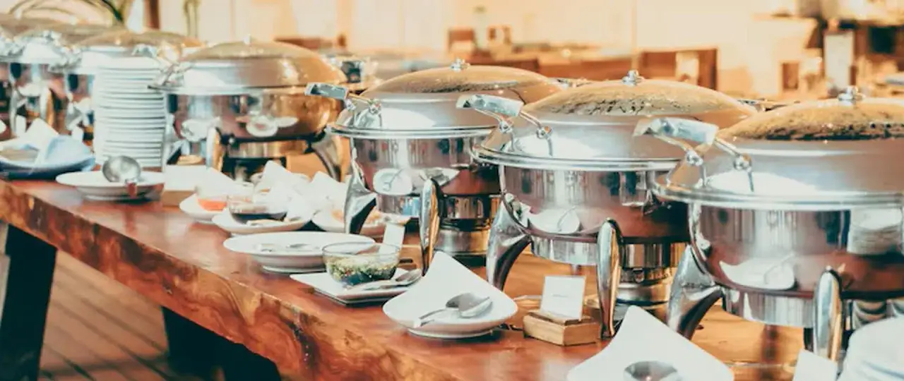 St&oacute;ł z podgrzewaczami do jedzenia, talerzami i sosami. Idealne wyposażenie, gdy zastanawiasz się, jak założyć firmę cateringową w domu.