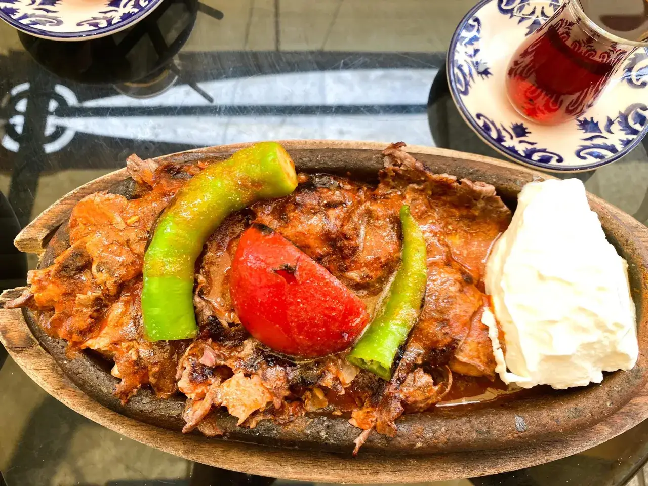 Pyszne tureckie jedzenie: mięso w sosie, pieczona papryka, pomidor i porcja jogurtu. Obok szklanka herbaty.