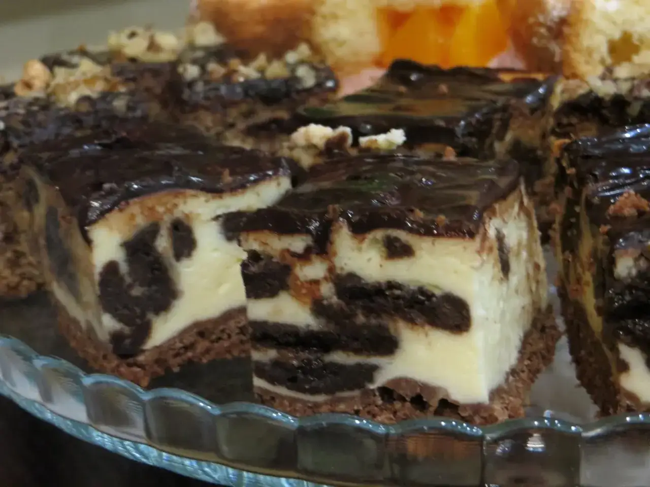 Pyszny, pieczony sernik Oreo z polewą czekoladową, pokrojony na kawałki, prezentuje się apetycznie na szklanej paterze.