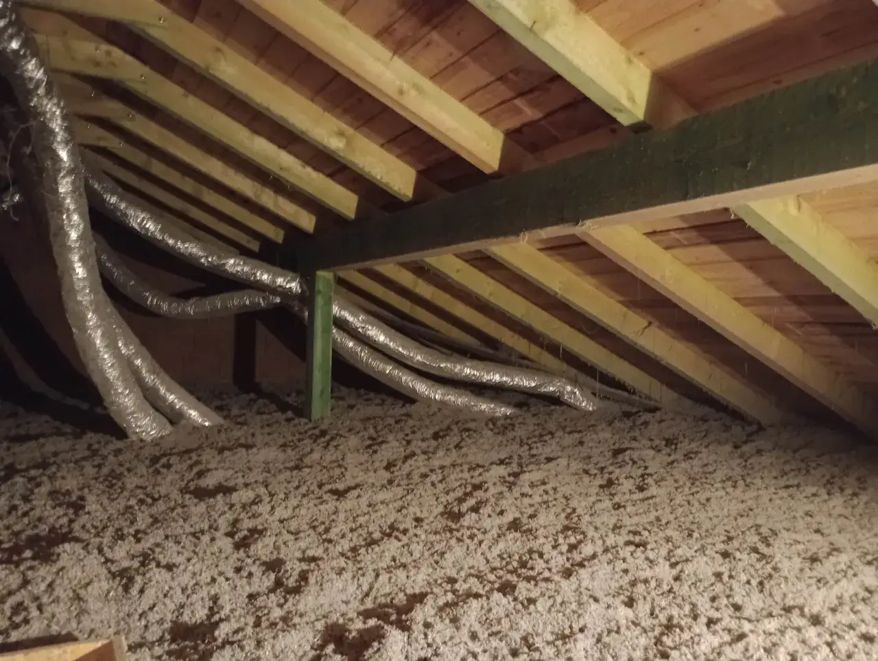 Warstwa izolacji na strychu, gotowa do dalszych prac, jak ocieplić strych. Widoczne przewody wentylacyjne i drewniana konstrukcja dachu.