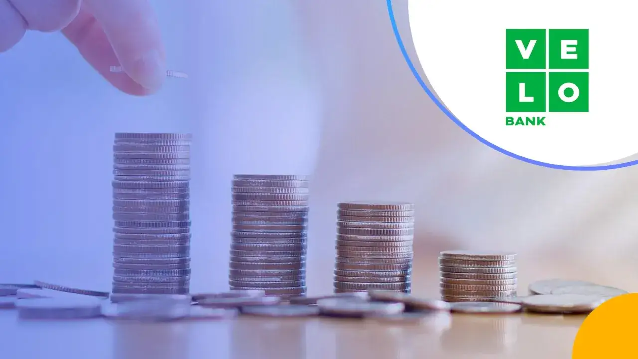 Ręka dodaje monetę do rosnącej stosu, symbolizując wzrost. Sprawdź atrakcyjne oprocentowanie konta walutowego w VeloBank.